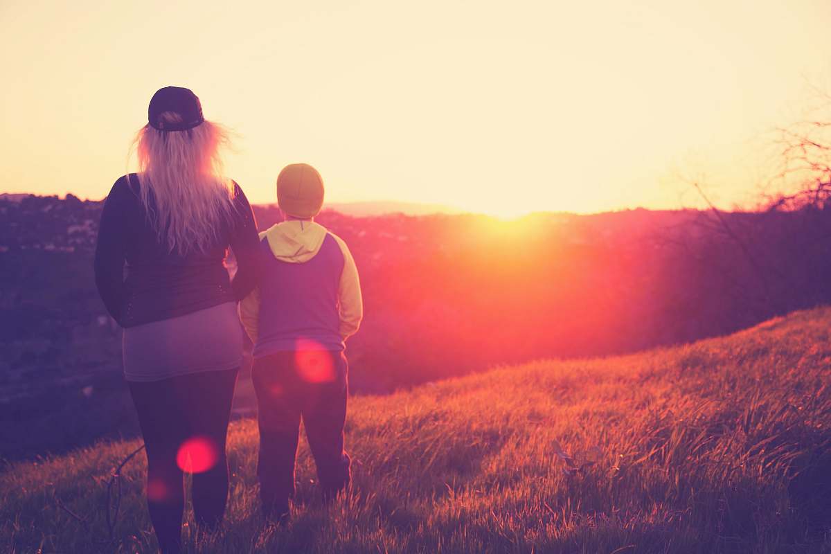 person silhouette photo of woman standing beside a child on grass field flare