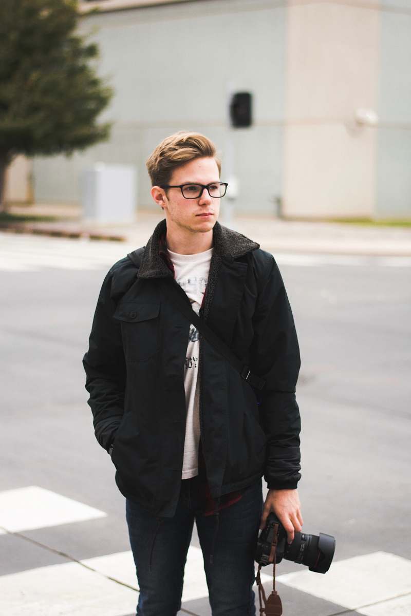 human standing man holding DSLR camera wearing eyeglasses and jacket person