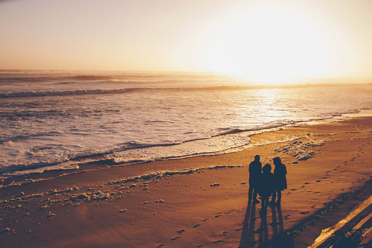 beach three people standing on sand near ocean during golden hour coast
