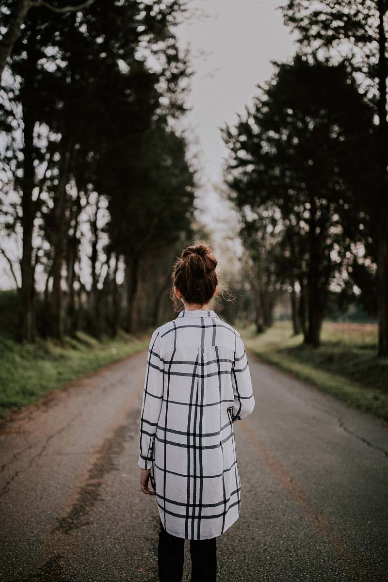 human tilt-shift lens photography of woman standing on gray road surrounded with trees person