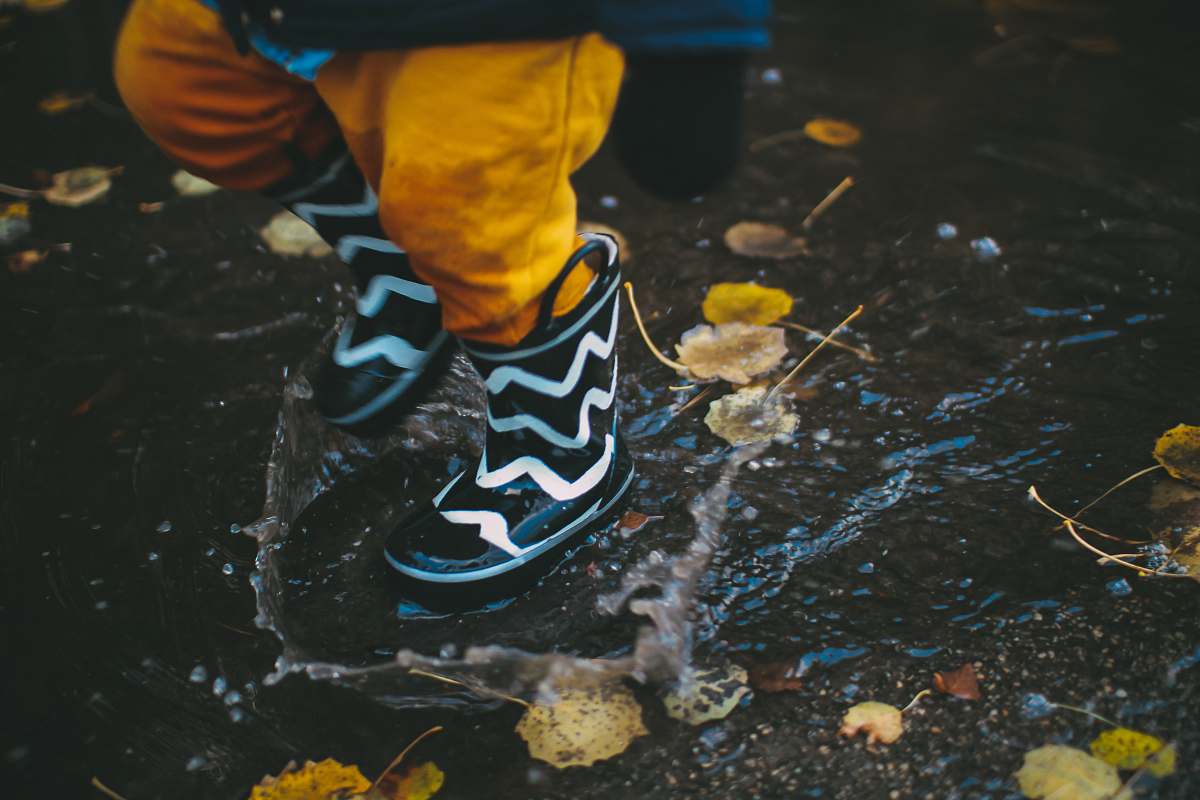 puddle toddler wearing black and white rain boots standing on body of water kid