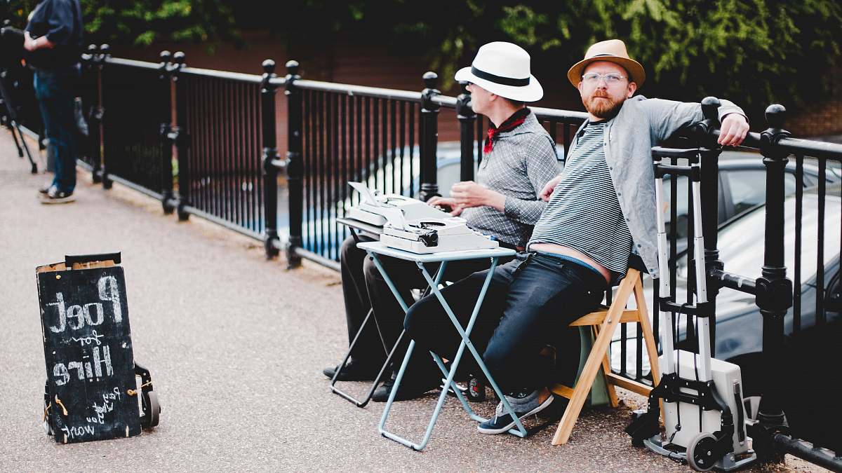 person two men sitting on bench while leaning on metal rail near poet hire signboard during daytime human