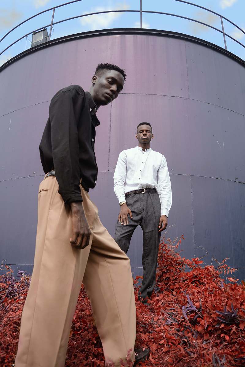 human two men standing on red flower in front of gray metal wall person