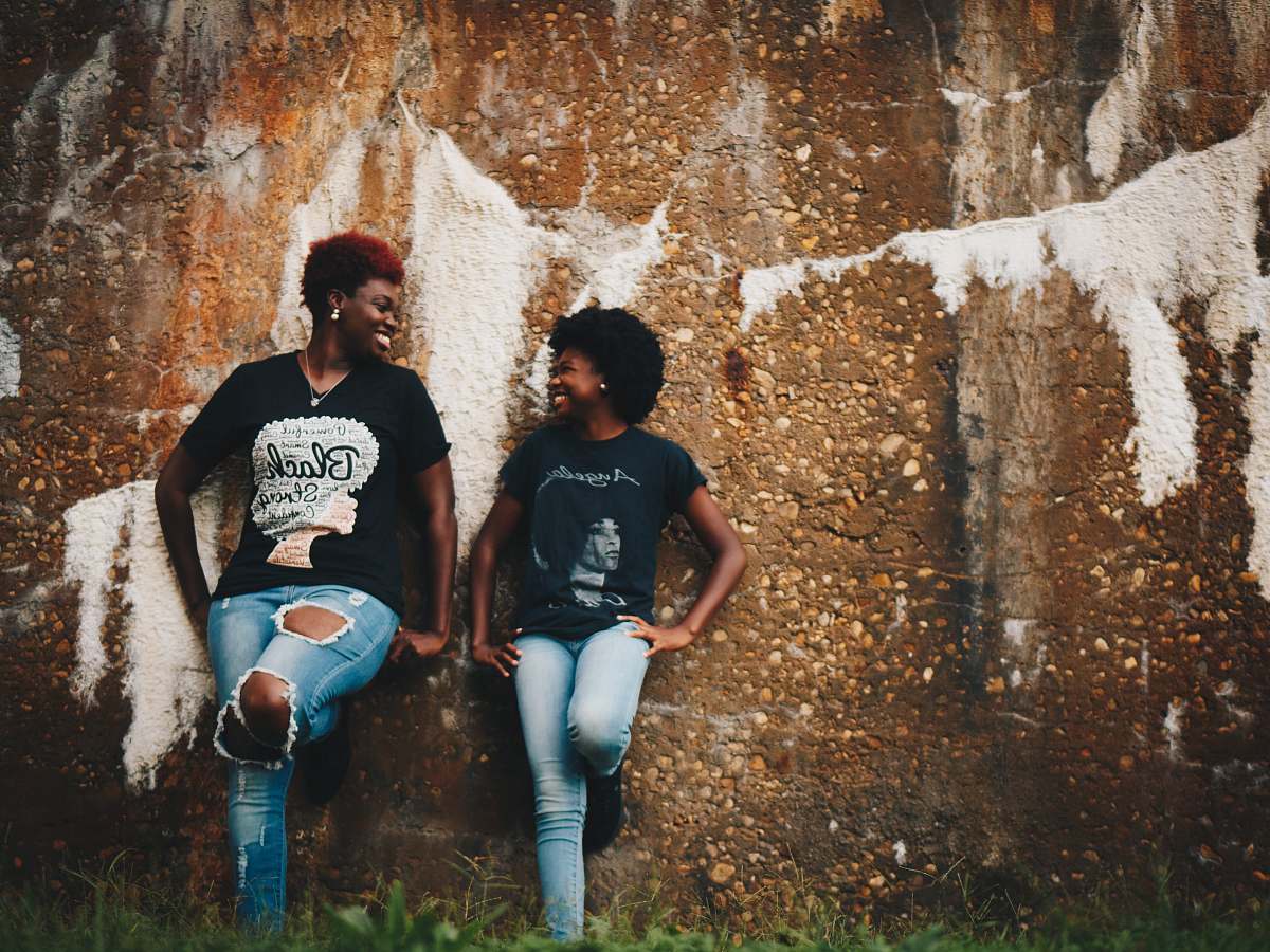 human two women standing behind brown wall person