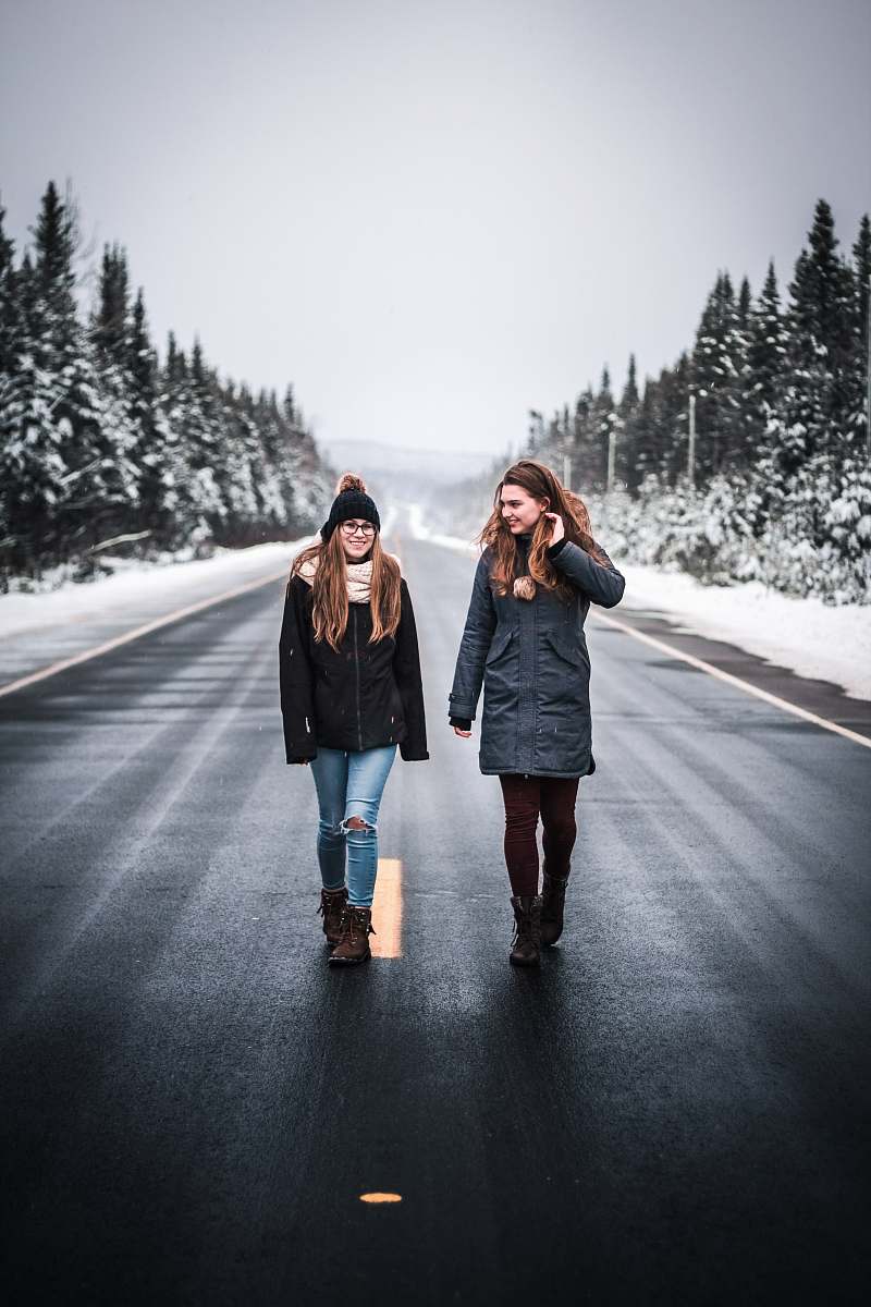 human two women walking on gray road between trees person