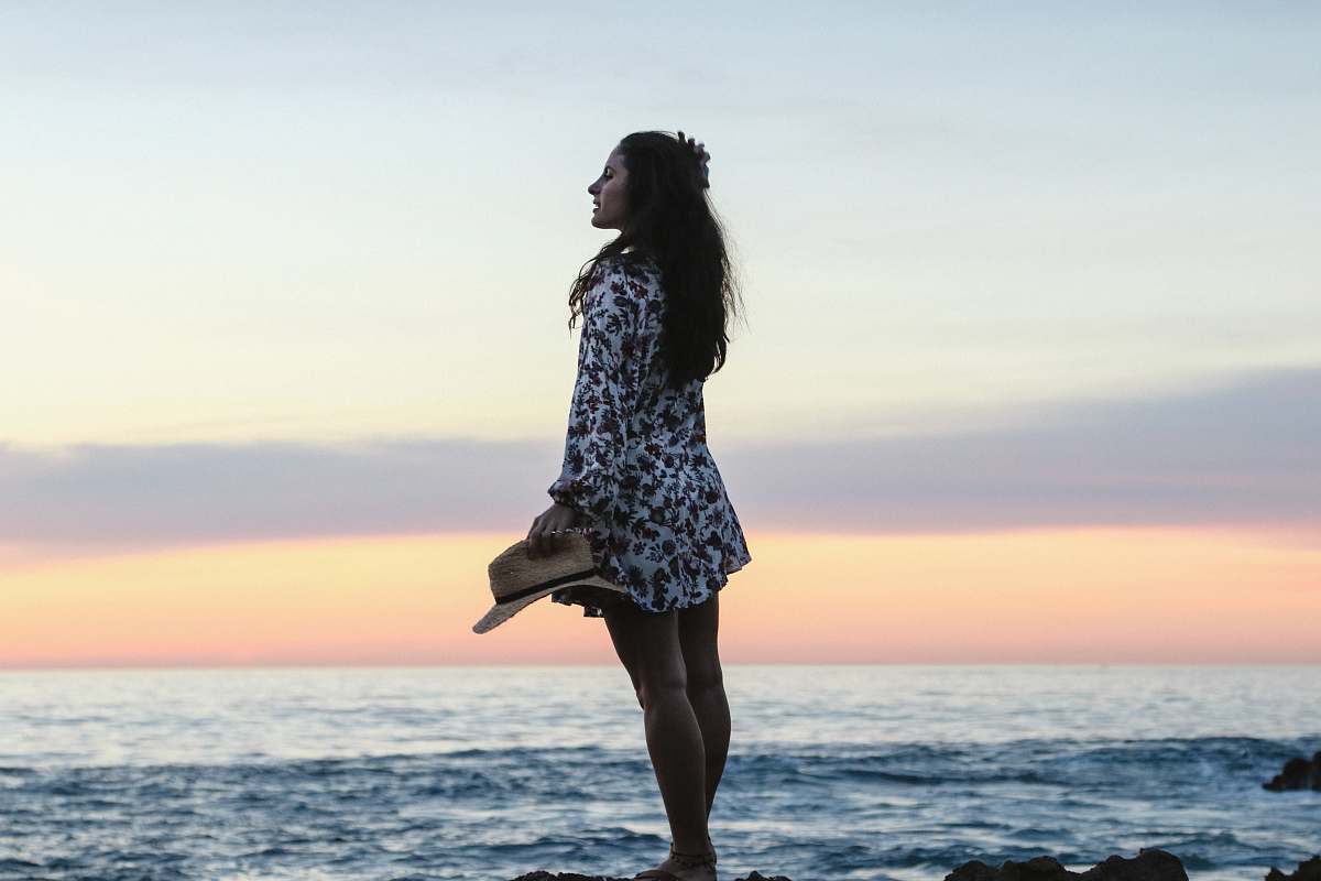 human woman holding brown sun hat on shore during sunset person