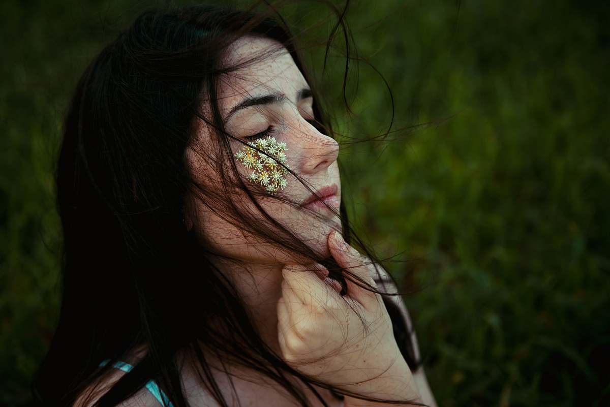 human woman holding chin with white petaled flowers on right cheek person