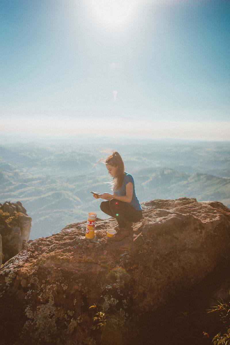 person woman holding smartphone while sitting beside orange bottle on top of rock formation human