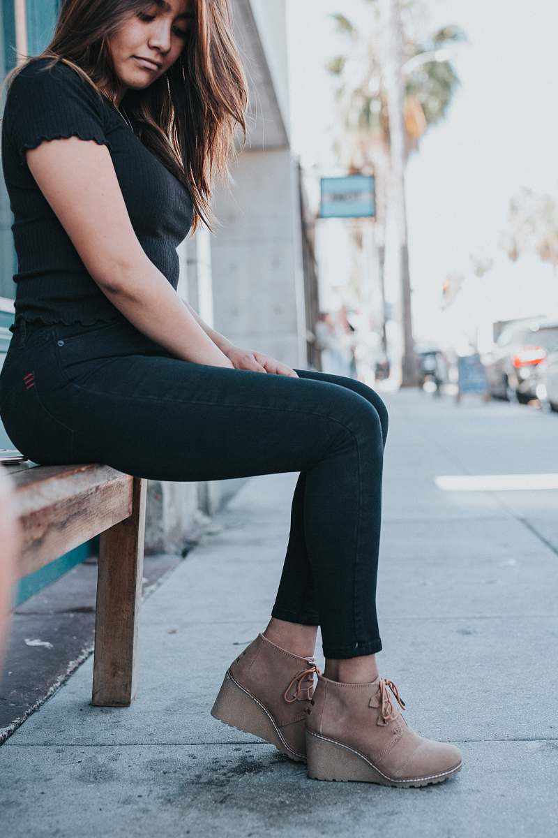person woman in black t-shirt and black pants sitting on brown wooden bench during daytime human