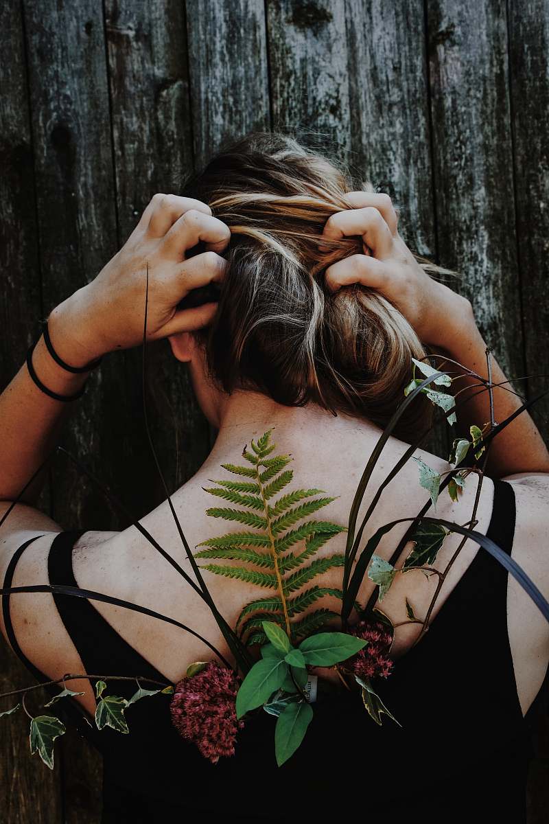 plant woman in black tank top with red petaled flower and assorted leaf on her back flora