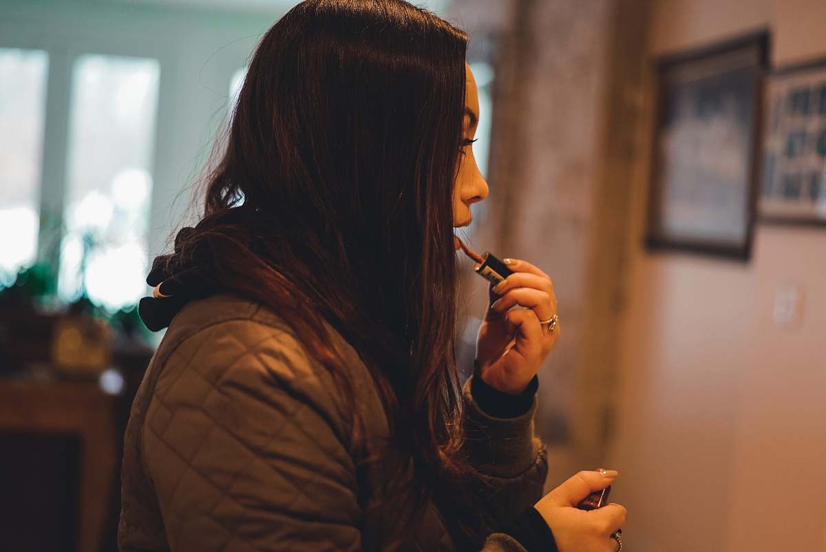 human woman in brown quilted hoodie holding lipstick shallow focus photography person