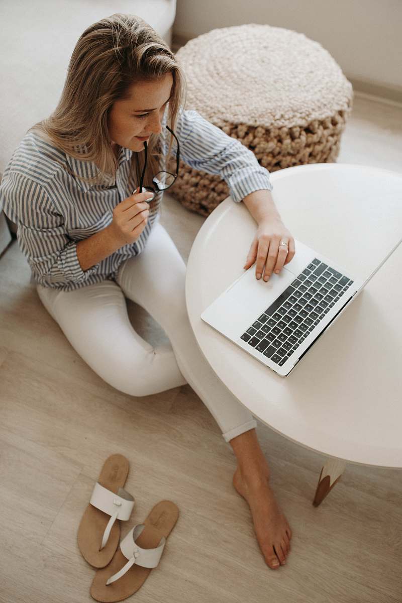 human woman in white and black striped dress shirt sitting on floor in front of table while using laptop computer person