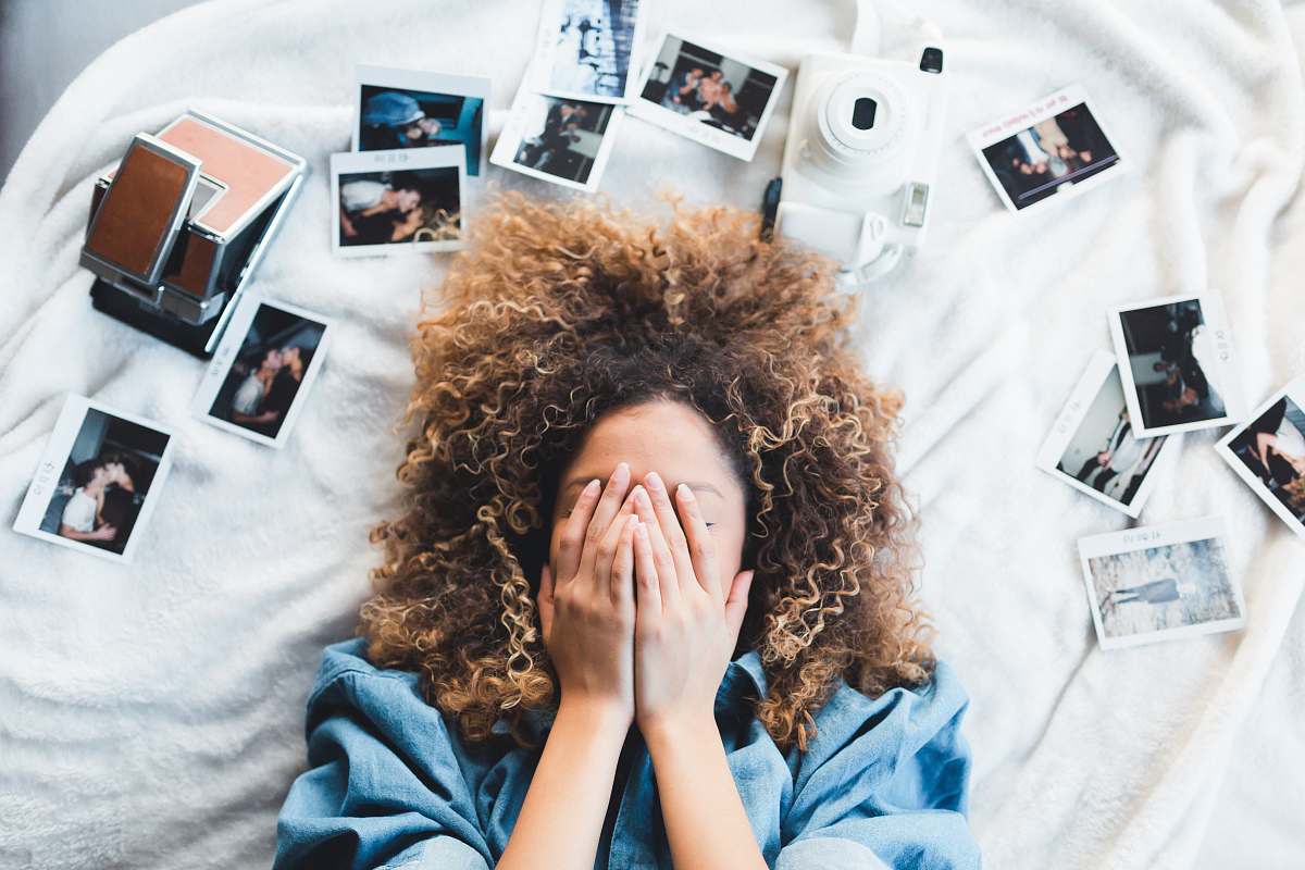 woman woman lying on bed covering her face surrounded by photos and white camera hair