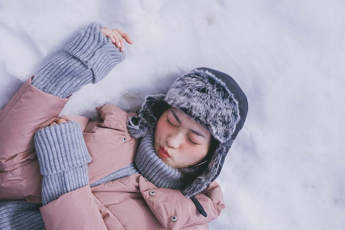 human woman lying on white snow during daytime person