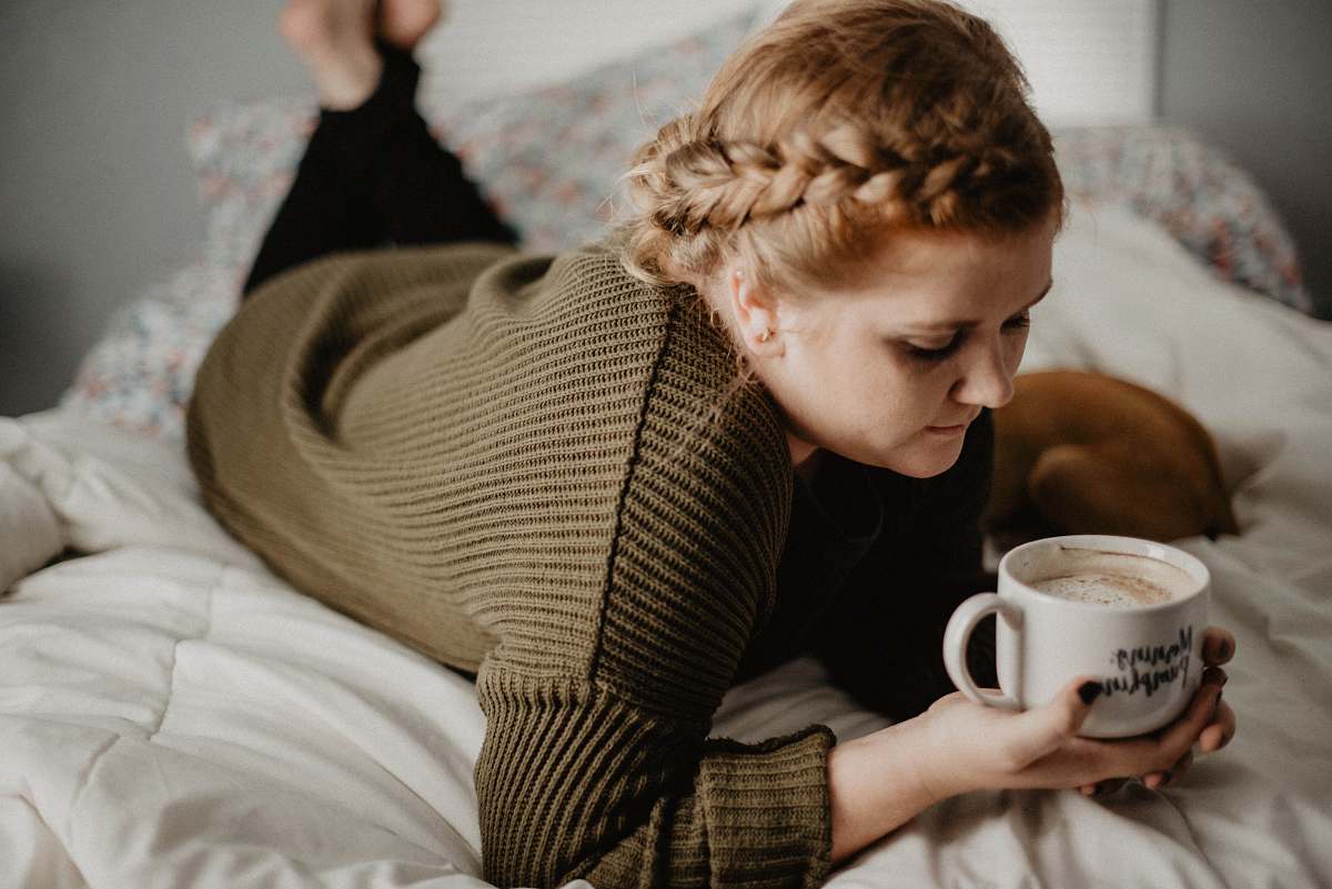 human woman on bed holding white mug person
