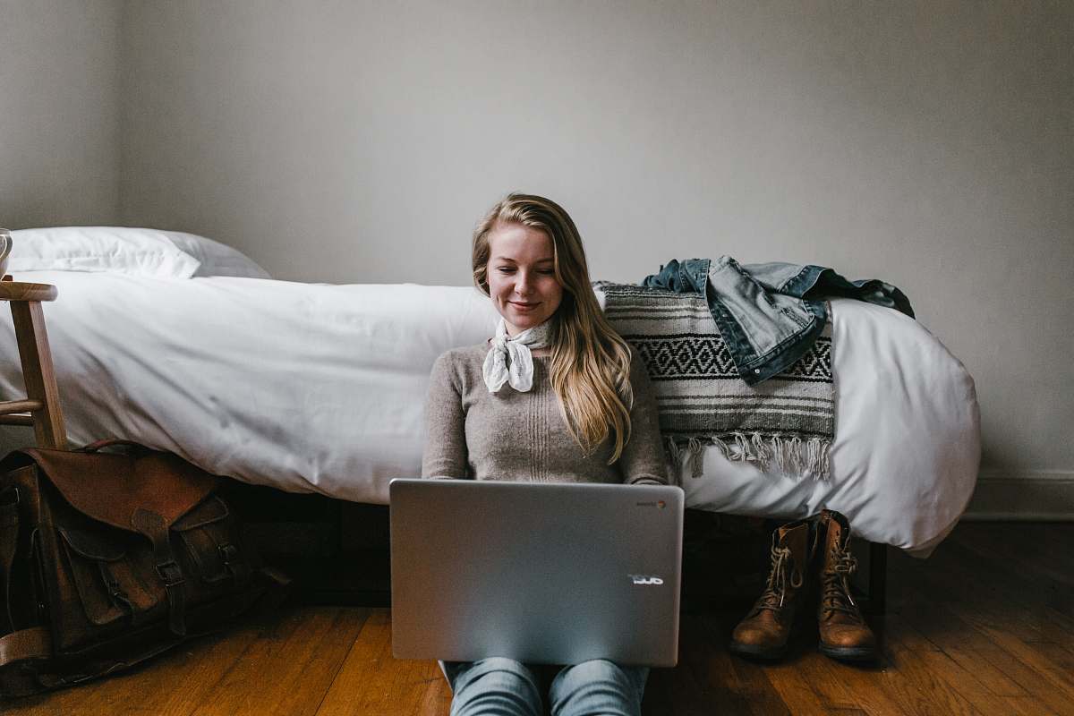 person woman sitting beside a bed while using a laptop human