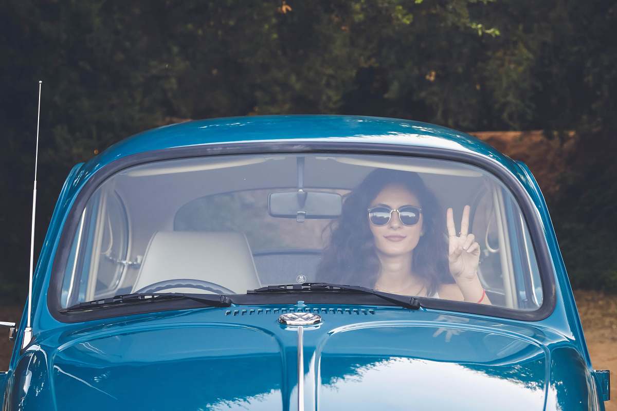 person woman sitting in passengers seat of blue Volkswagen Beetle and performing peace sign windshield