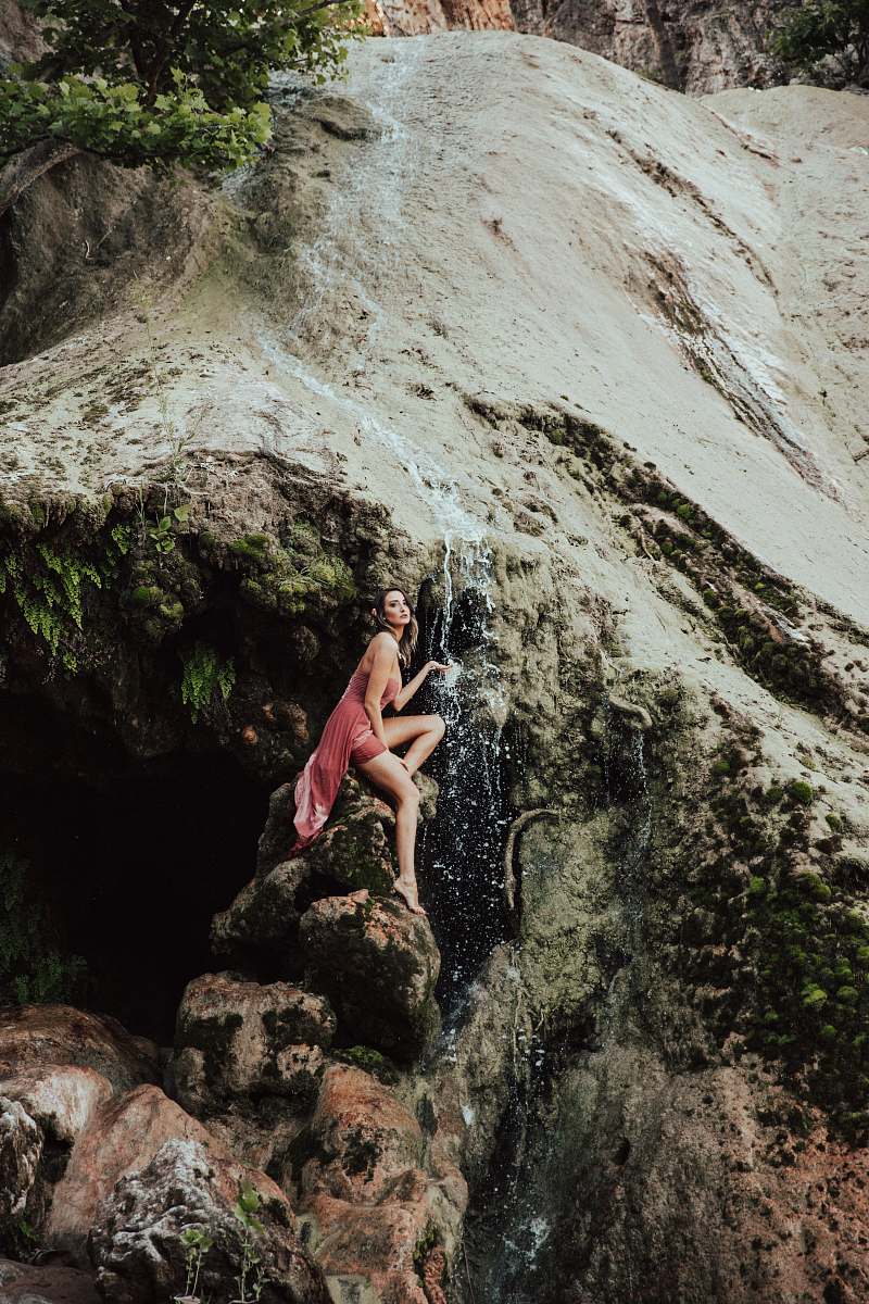 human woman sitting on rock under waterfalls person
