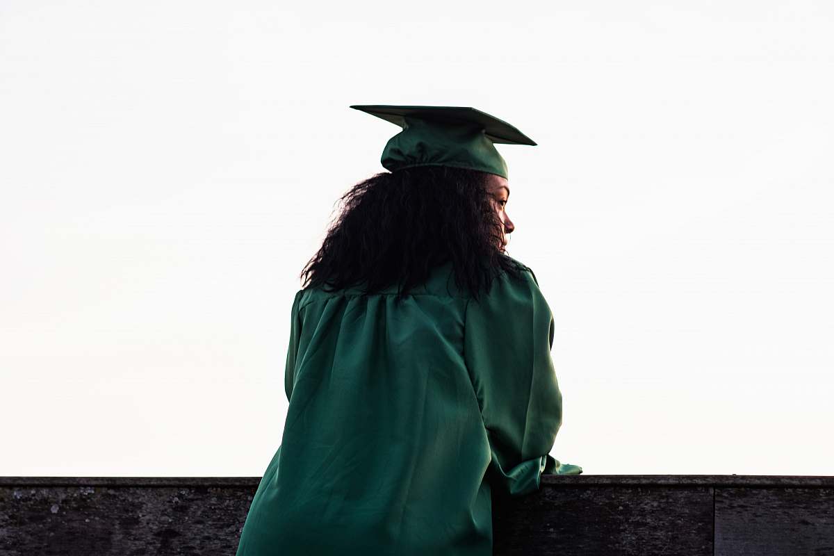 person woman standing at front of concrete fence wearing academic uniform human