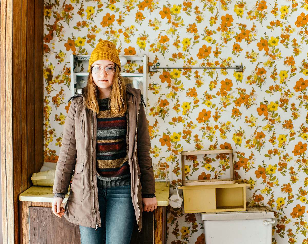 human woman standing near cabinet in front of floral wallpaper person