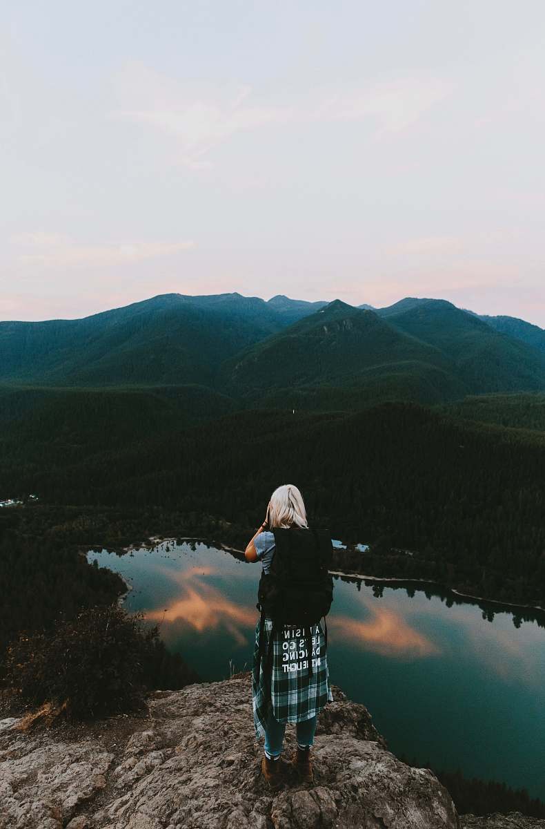 human woman standing on cliff taking picture of mountain person