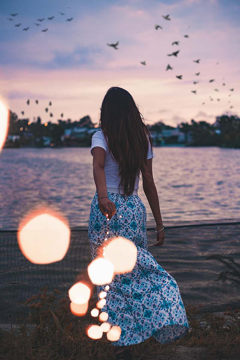 person woman standing on green grass field in front body of water under flock of birds human