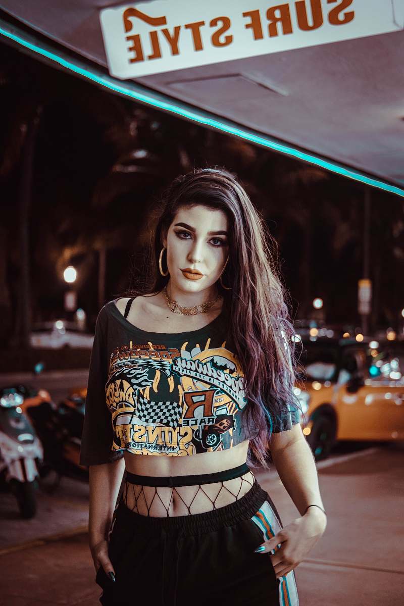 human woman wearing black crop top standing near surf style signage looking straight person