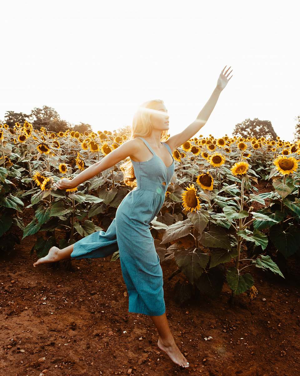 human woman wearing green sleeveless rompers standing and waving hands near garden of sunflower at daytime flower