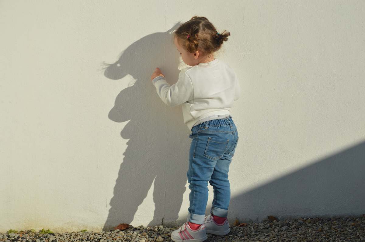 human child touching white painted wall during daytime people