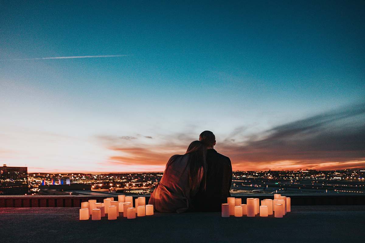 people couple sitting on the field facing the city human