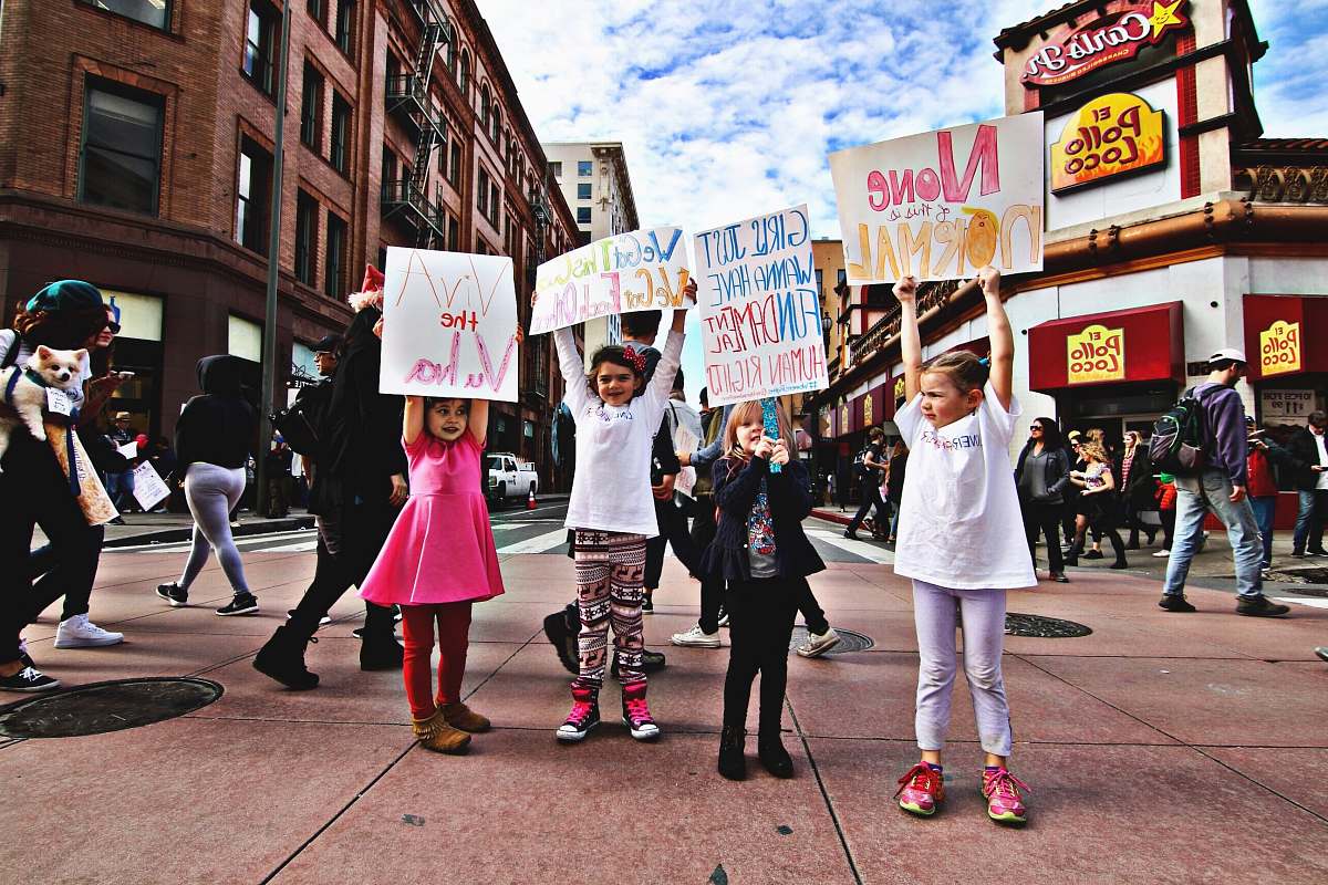 people four children raising up a banner at the middle of a busy street during day time signs