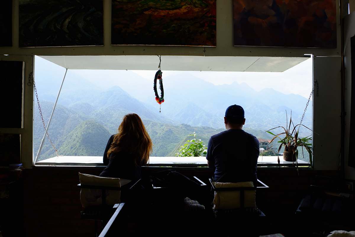 Capture the essence of tranquility with this stunning image of a man and woman seated together in a cozy room, gazing out a large window that frames a breathtaking mountain landscape. Perfect for illustrating themes of romance, adventure, and connection to nature, this photograph evokes feelings of peace and reflection, making it ideal for use in travel blogs, relationship articles, or interior design projects that highlight beautiful views.