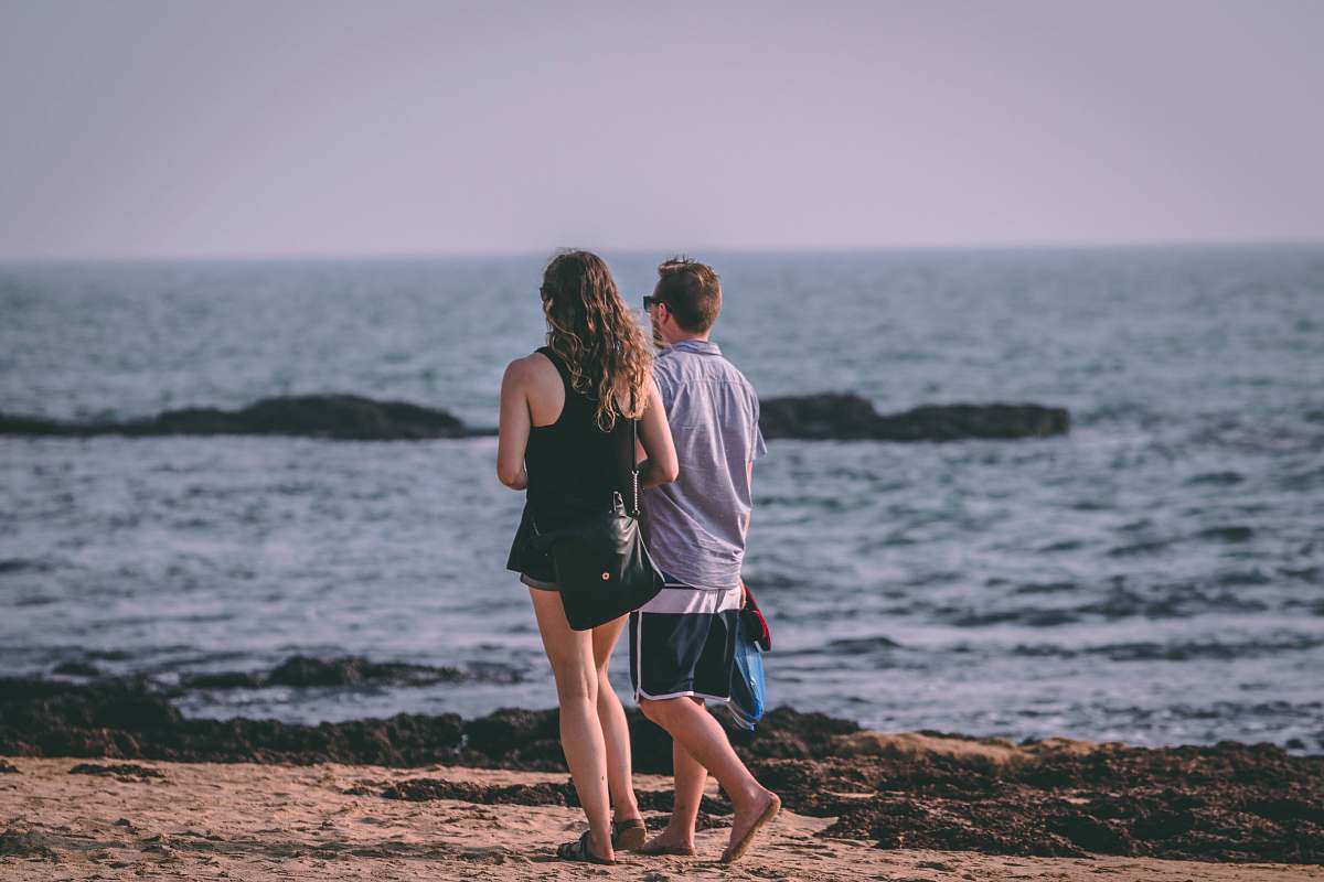 human man and woman walking by the beach during daytime people