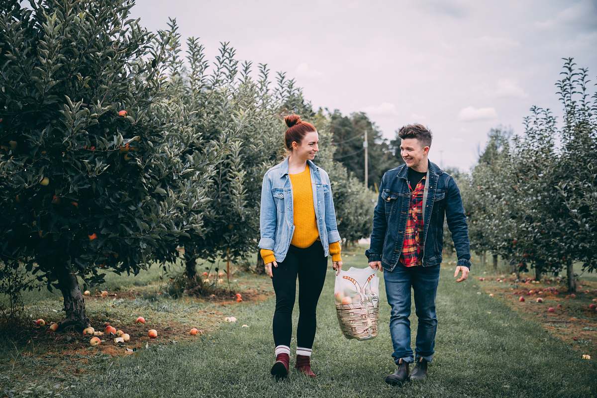 human man carrying bag with woman in fruit tree orchard at daytime people
