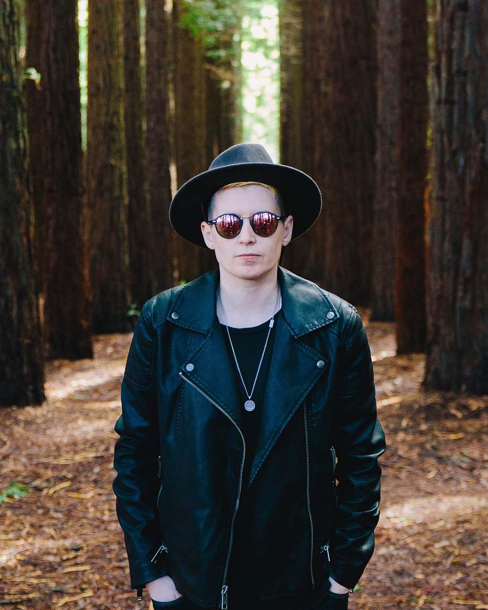 human man in black full-zip jacket standing between green trees man
