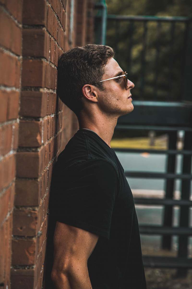 human man in black short-sleeved shirt leaning on brow brick wall leaning