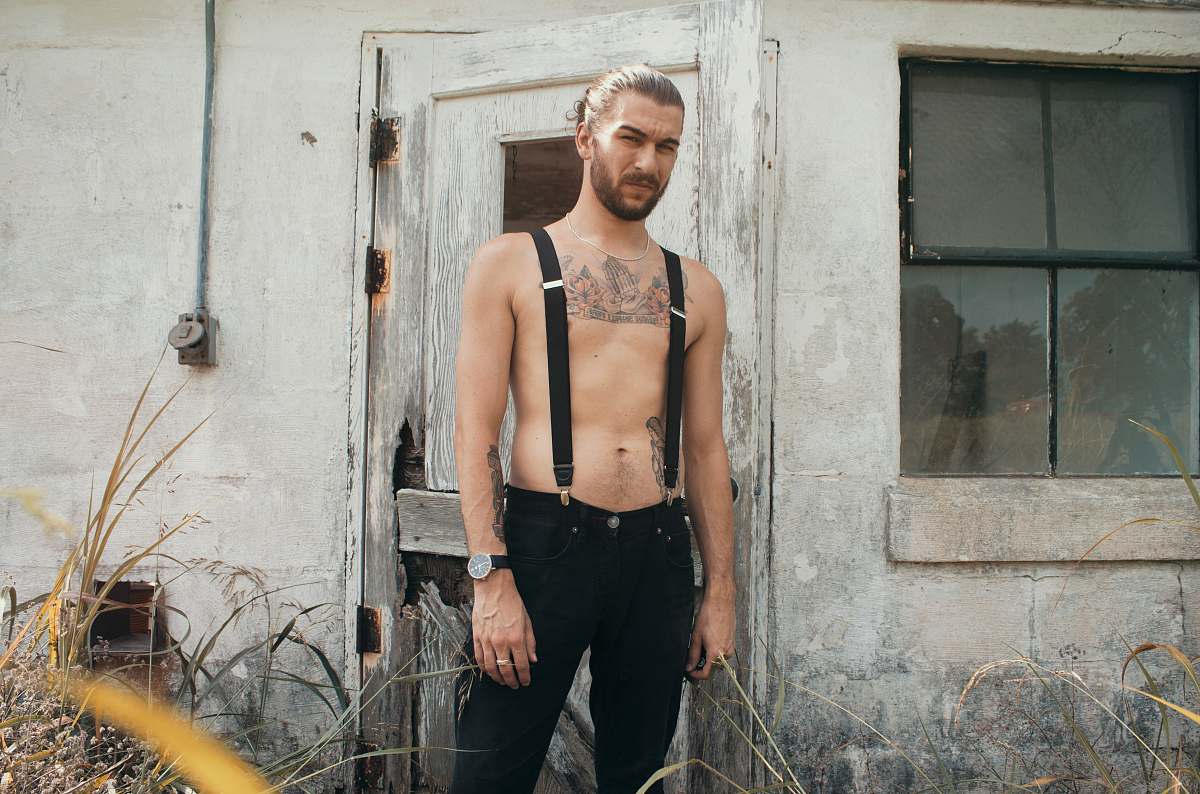 human man in black suspender belt standing in front of gray house people