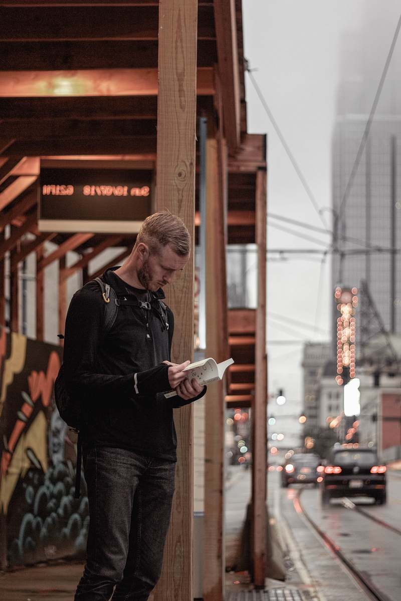 people man in black sweater stands on sidewalk with book in hand human