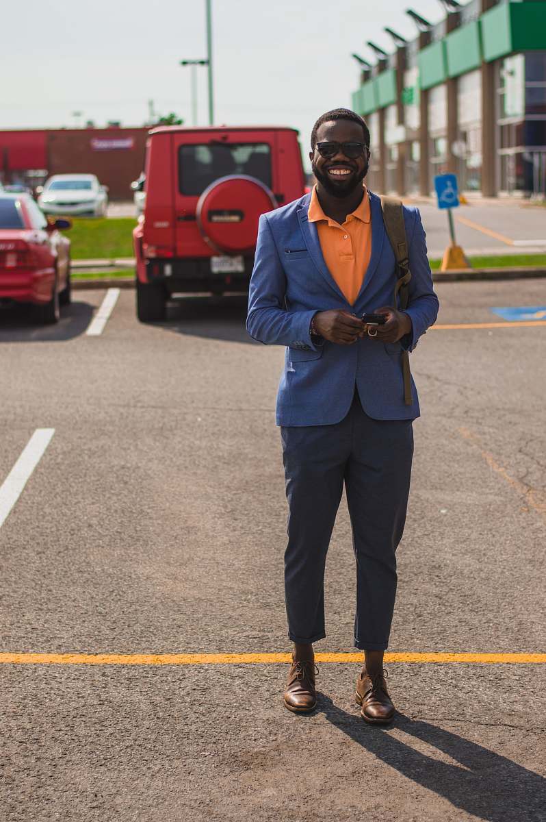 human man in blue suit jacket standing at the back of red car people
