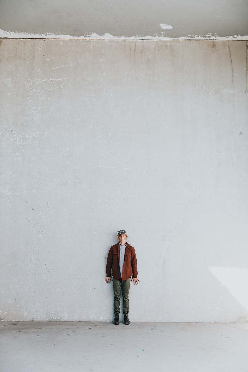 human man in brown coat standing by the white wall people