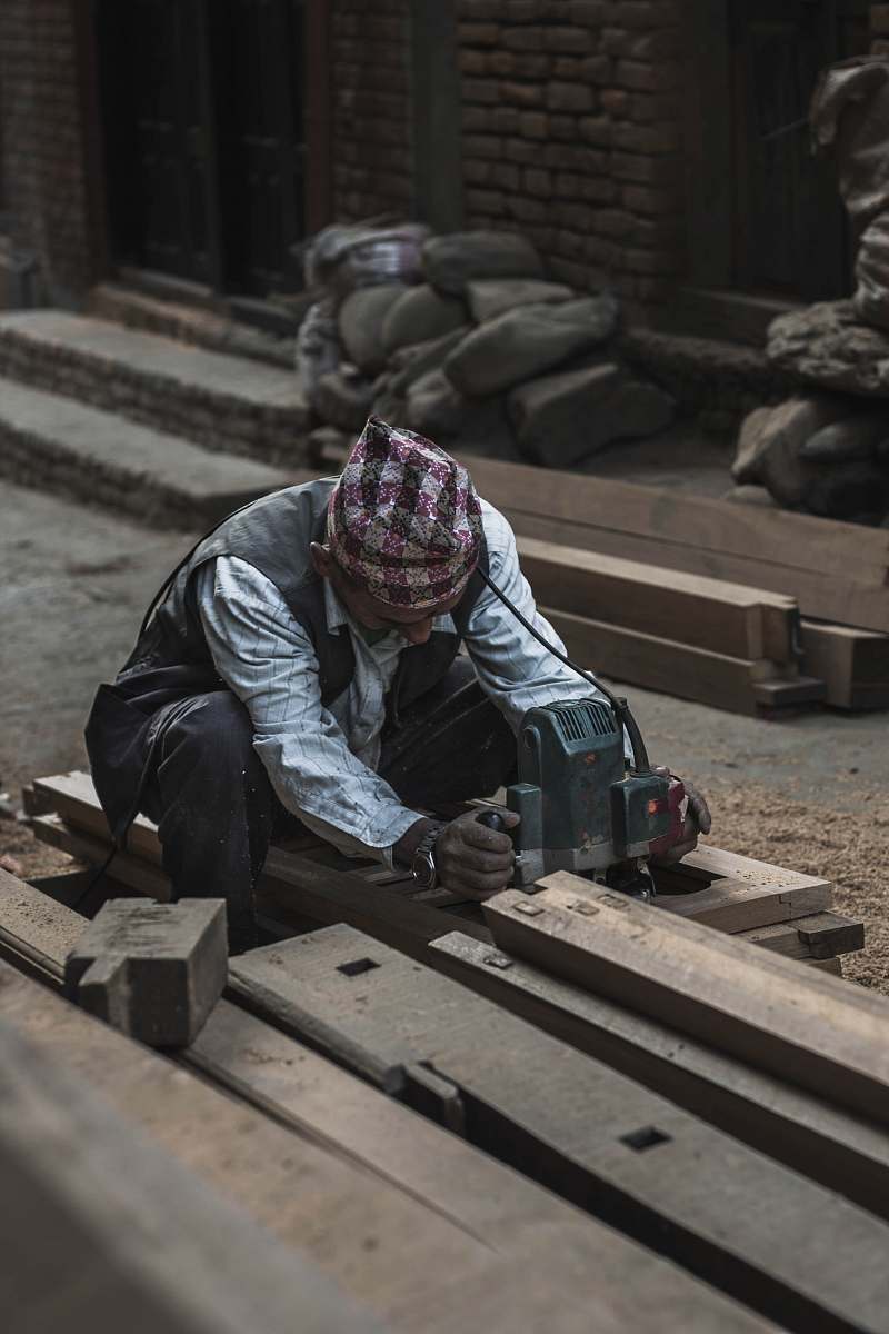 people man in white striped shirt sitting on brown pallet holding gray power tool human