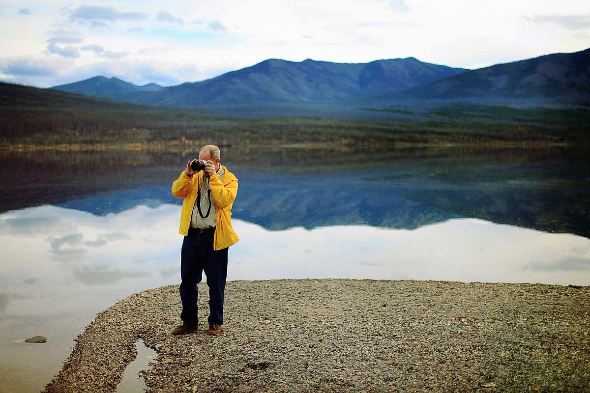 human man in yellow jacket taking pictures during daytime people
