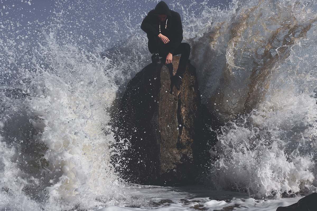 sea man seating on stone in between waving sea ocean