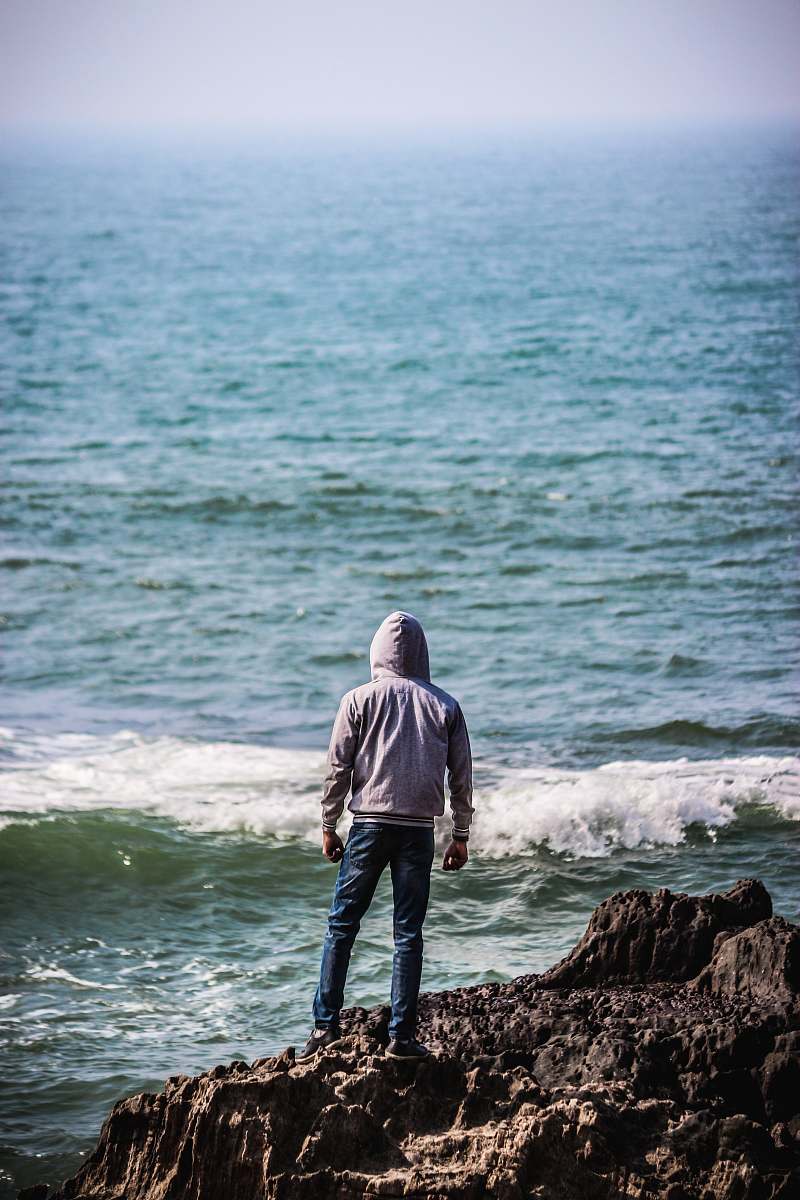 human man standing on cliff facing body of water people