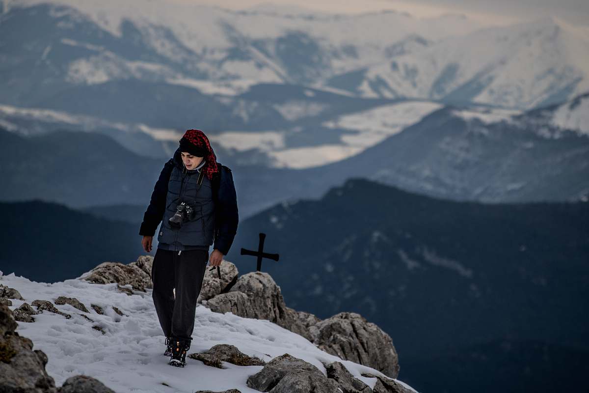 human man standing on peak near cross at daytime people