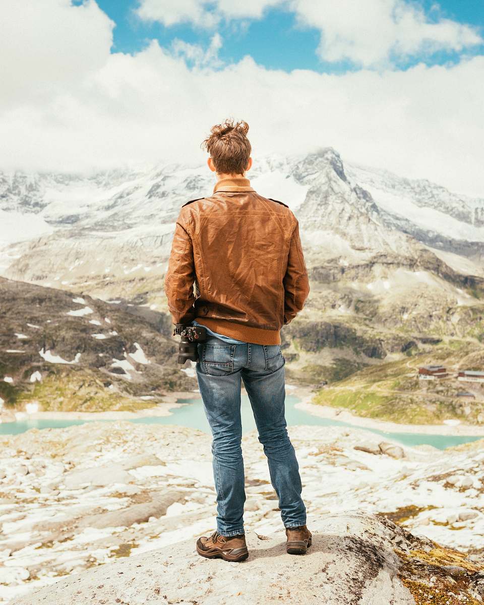 people man standing on rock facing lake and mountains during daytime human