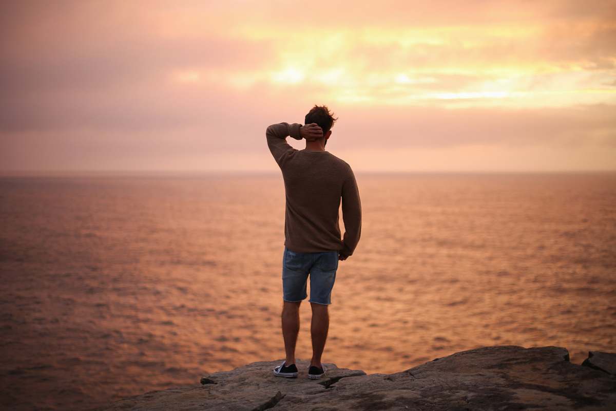 human man standing on rock near seashore during sunset people