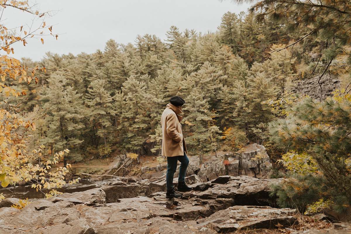 people man standing on rocky cliff surrounded with trees during daylight human