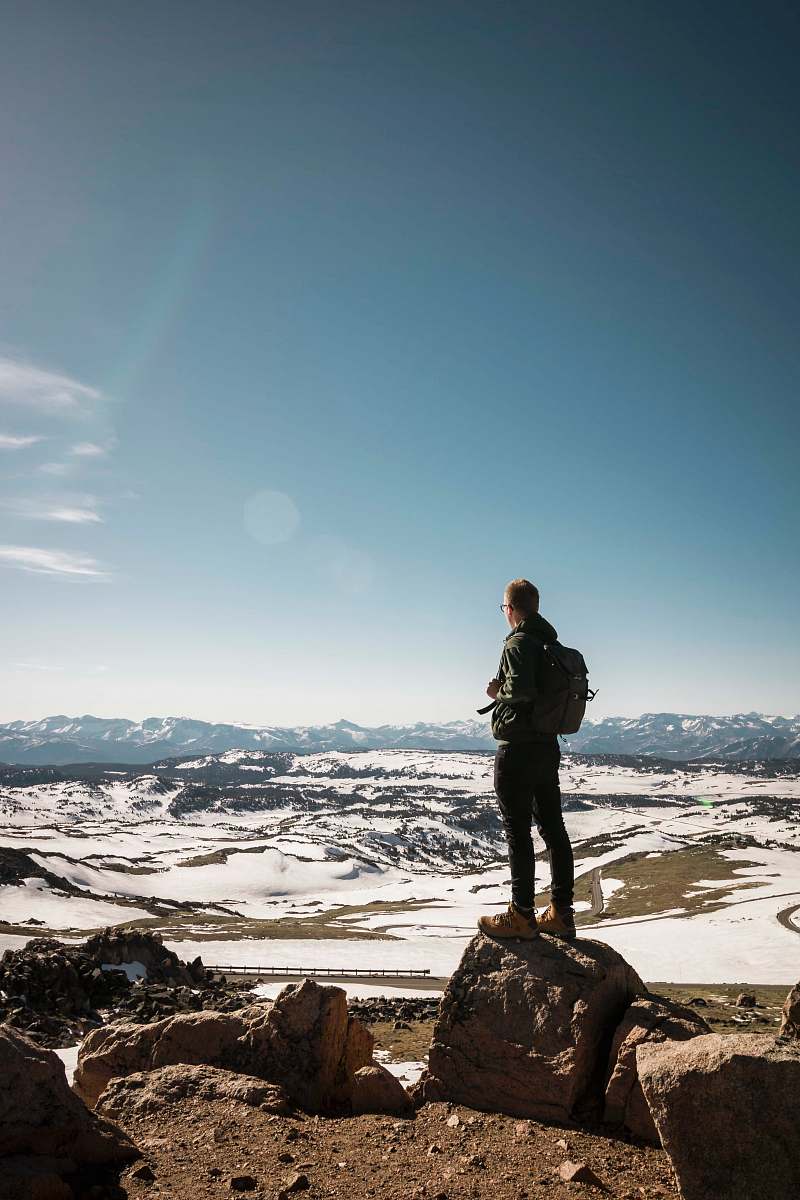 human man standing on stone overlooking snow-capped mountain people