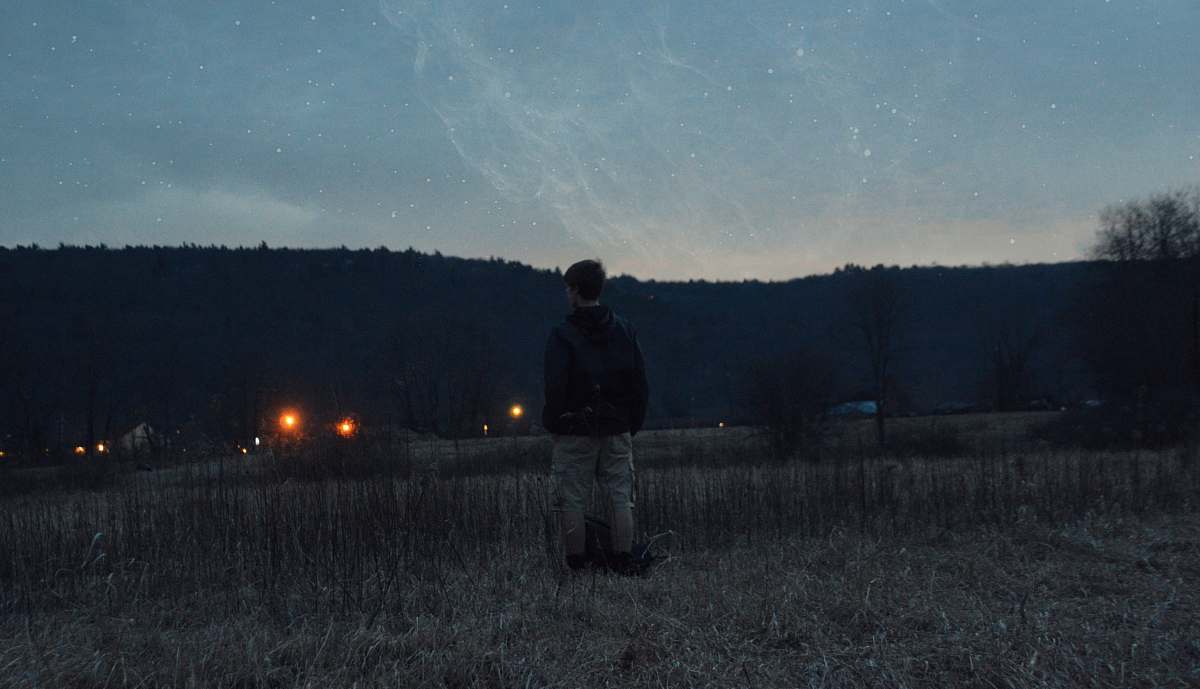 stars man wearing black jacket standing near grass looking at mountain field